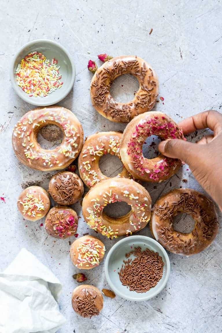 A variety of Air Fryer Donuts next to small bowls filled with sprinkles and dried edible flowers