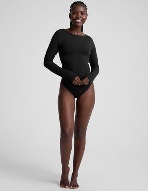 woman wearing a black long-sleeve boatneck bodysuit on a plain background. 