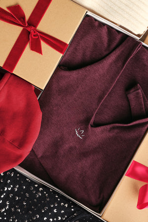 Maroon garment with a brand logo in an open gift box with red ribbon. 