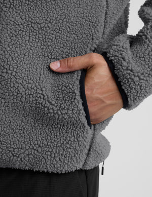 man wearing a gray fleece zip-up jacket against a plain background. 