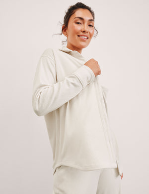 Woman wearing a white corduroy button up shirt and white corduroy pants with a plain background. 