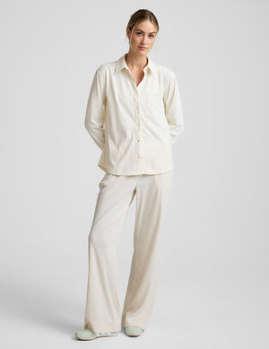 Woman wearing a cream-colored corduroy button up shirt and pants on a plain background. 