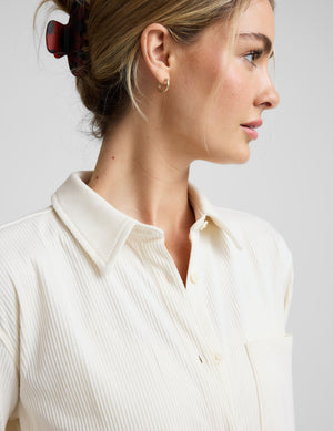 Woman wearing a cream-colored corduroy button up shirt and pants on a plain background. 