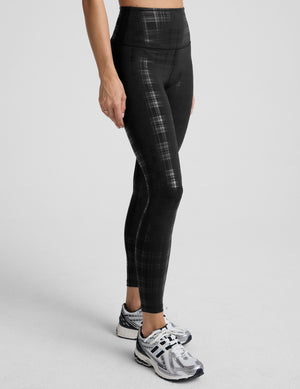 model wearing black plaid foil leggings on a white background. 