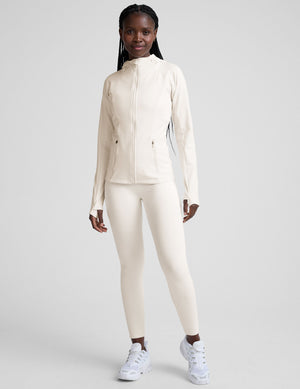 woman wearing a white athletic hooded jacket and leggings on a plain background. 