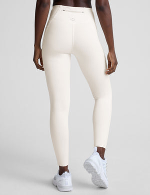 woman wearing white high-waisted long length leggings with pockets on a plain background. 