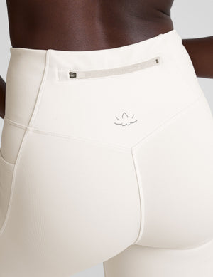 woman wearing white high-waisted long length leggings with pockets on a plain background. 