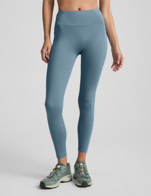 Woman wearing a blue fleece lined blue leggings with pockets on a light gray background. 