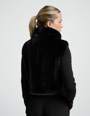 woman wearing a black faux fur vest against a plain background. 