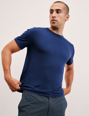 Man wearing a blue t-shirt and gray pants against a plain background. 