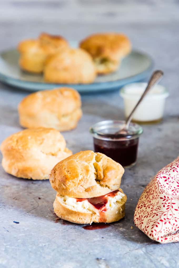 lemonade scones scattered on countertop with jam and whipped cream on closest scone