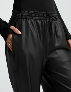 woman wearing a black long sleeve with wide-leg faux leather pants against a plain background. 