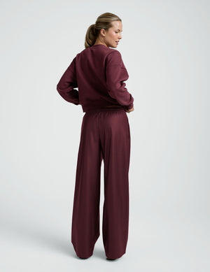 woman wearing a red sweatshirt and red faux leather wide leg pants against a plain background. 