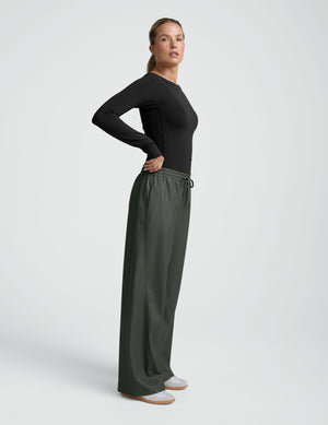 woman wearing a black long sleeve and green wide-leg faux leather pants against a plain background. 