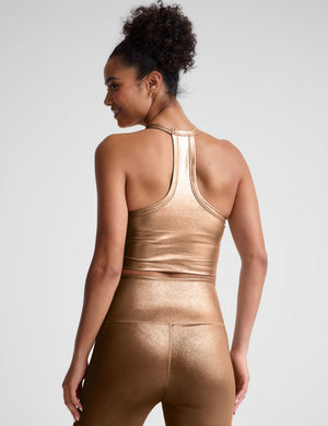 woman wearing a gold cropped v neck tank on a plain background. 