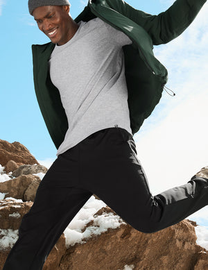 man in outdoor setting with snow and rocks, wearing a green jacket and gray shirt.