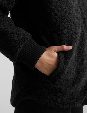 Woman wearing a black quilted and boucle jacket on a light gray background. 