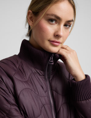 Woman wearing a quilted and boucle purple jacket on a light gray background. 
