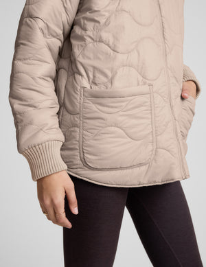 Woman wearing a beige quilted and boucle jacket on a light gray background. 