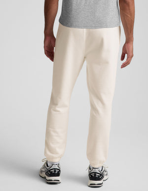 man wearing a gray crew neck t-shirt and white fleece sweatpants on a plain background. 