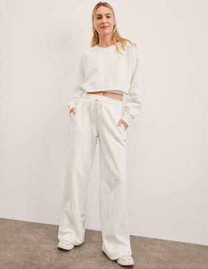 model wearing a white crew neck sweatshirt and white fleece wide leg pants against a plain background. 
