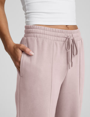 Woman wearing a white tank top and pink fleece pintuck pants against a plain background. 