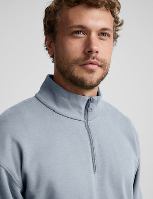 Man wearing a light blue half-zip sweatshirt against a plain background.