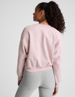 woman wearing a light pink sweatshirt and gray leggings on a plain background. 