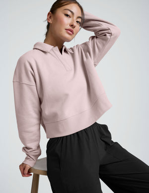 woman wearing a light pink collared sweatshirt and pants on a plain background. 