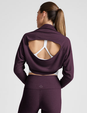 model wearing a white cropped tank and purple leggings with a purple shrug on a light background. 