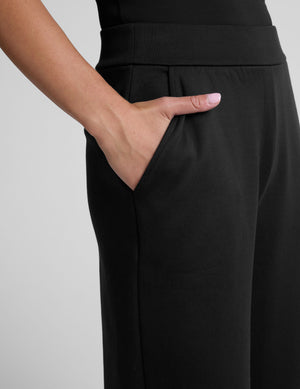 model is wearing a black sleeveless top and black spacer style pants with pockets against a plain background. 