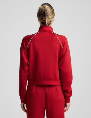 Woman wearing a red jacket with white piping against a plain background. 