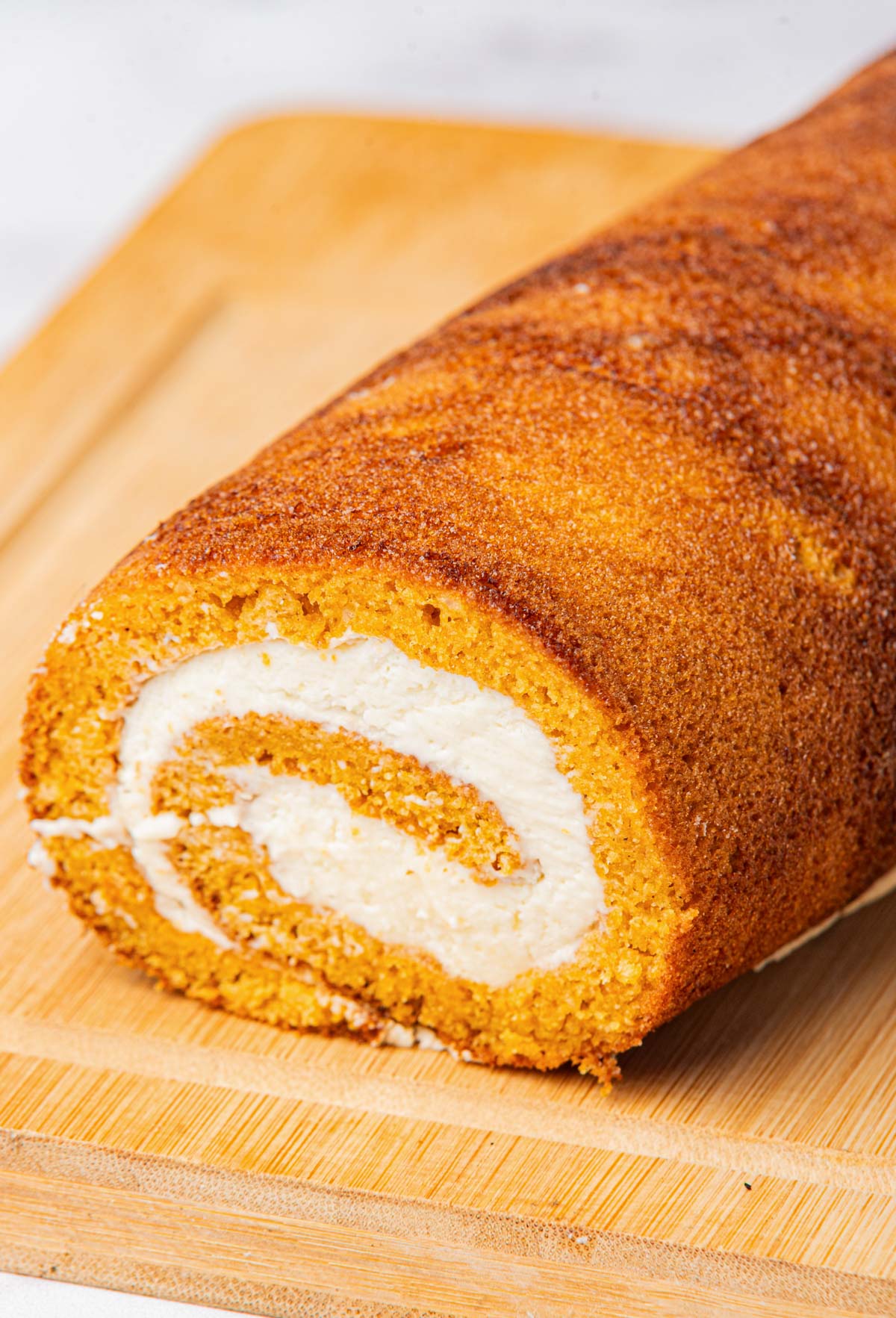Close-up of a finished pumpkin roll with cream cheese filling on a wooden cutting board.