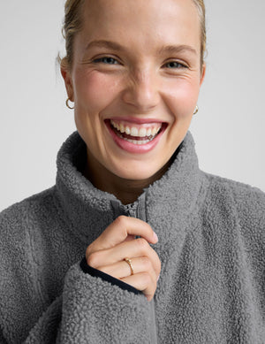 model wearing a gray fleece zip-up jacket against a plain background. 