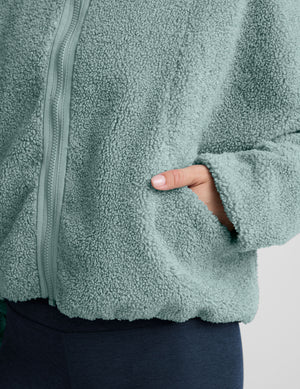 model wearing a blue zip-up fleece jacket against a plain background. 