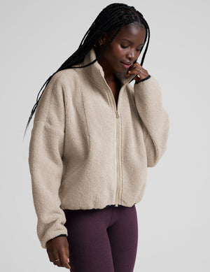 model wearing a beige zip-up fleece jacket against a plain background. 