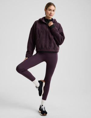 Woman wearing a purple quarter zip boucle jacket against a plain background. 