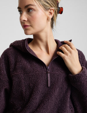 Woman wearing a purple quarter zip boucle jacket against a plain background. 