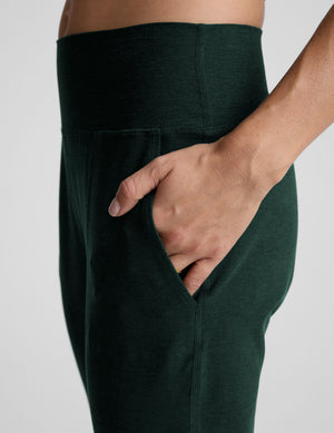 person wearing dark green jogger pants and white sneakers on a plain background. 