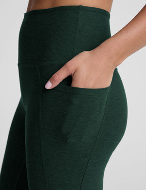 model is wearing green high-waisted midi length leggings with pockets on a plain background.