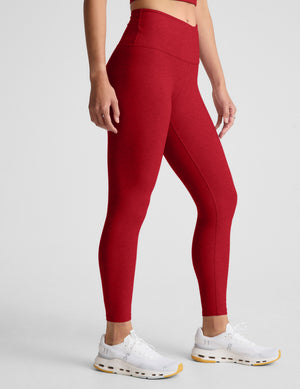 woman wearing red high-waisted midi length leggings with an overlapping waistband against a plain background. 