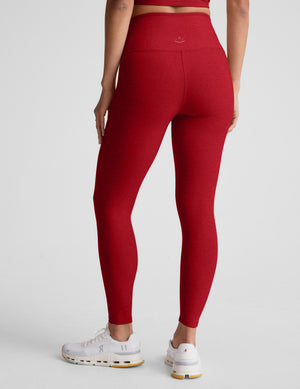 woman wearing red high-waisted midi length leggings with an overlapping waistband against a plain background. 