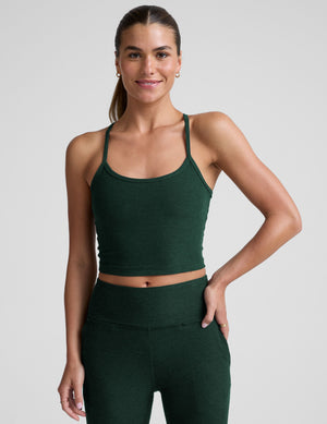 woman wearing a green racerback cropped tank top and pants against a plain background. 
