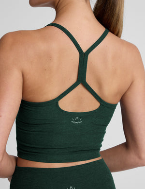 woman wearing a green racerback cropped tank top and pants against a plain background. 