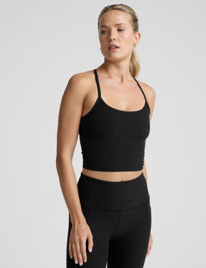 woman wearing a black racerback cropped tank and leggings on a plain background. 
