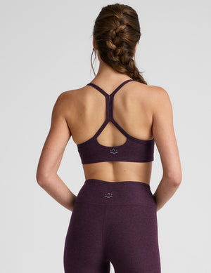 Woman wearing a purple slim racerback bra and leggings on a light gray background. 