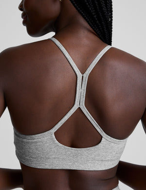 model is wearing a gray racerback bra with slim spaghetti straps and leggings against a plain background. 