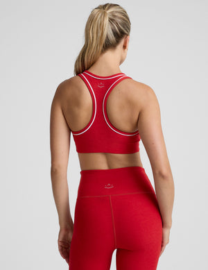 Woman wearing a red sports bra and leggings with white piping on a light background. 