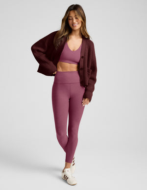 Woman wearing a maroon cardigan and leggings against a light gray background.