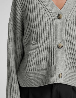 woman wearing a gray ribbed cardigan on a plain background. 